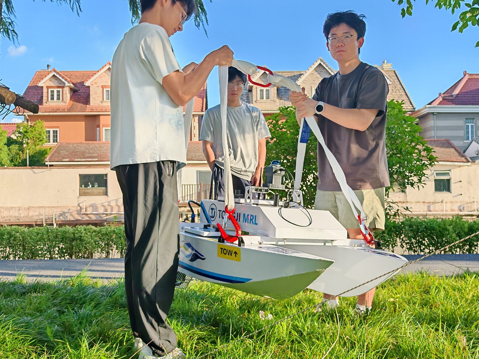Three team members fitting lifting straps to the USV beside the water